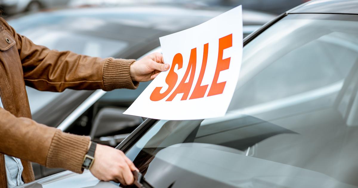 Vendedor poniendo placa de venta en el auto