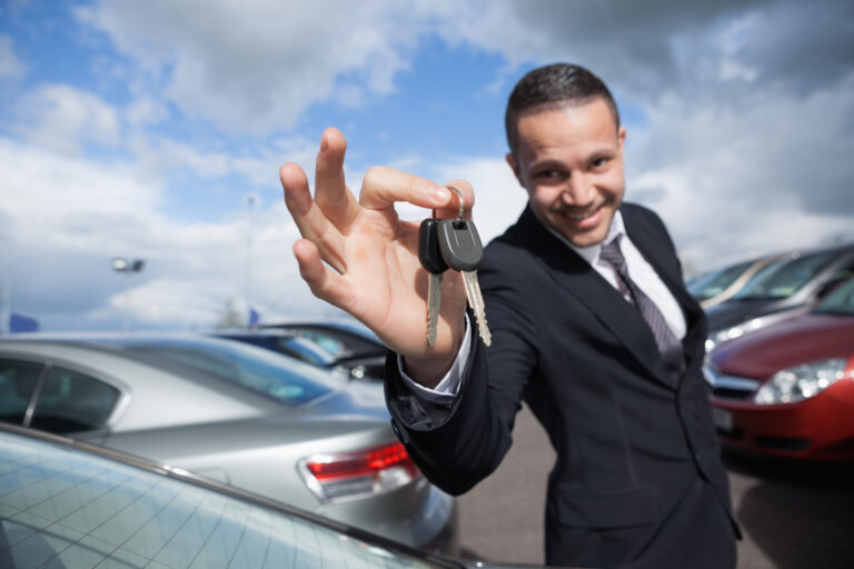 Happy dealer holding car keys outdoors